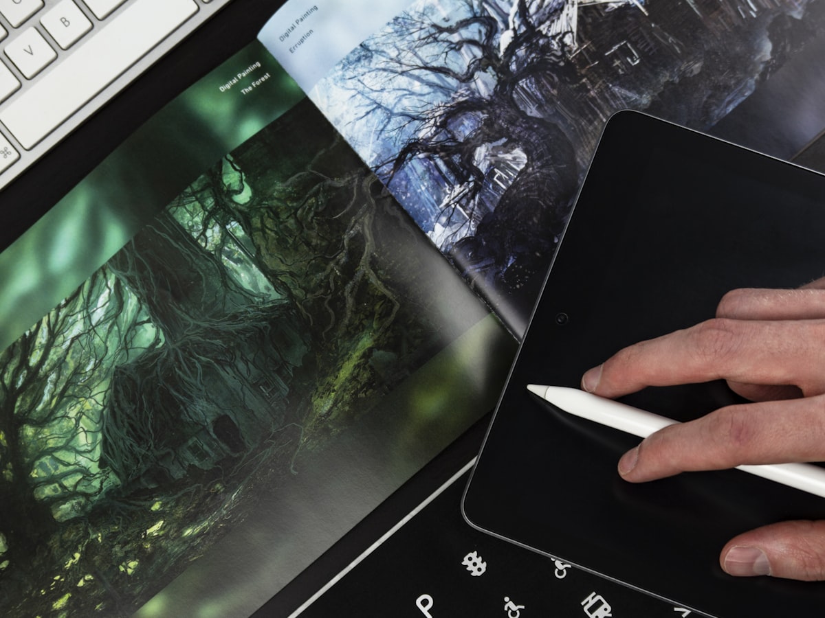 A hand holding a stylus over a tablet, resting on printed digital-painting artwork.