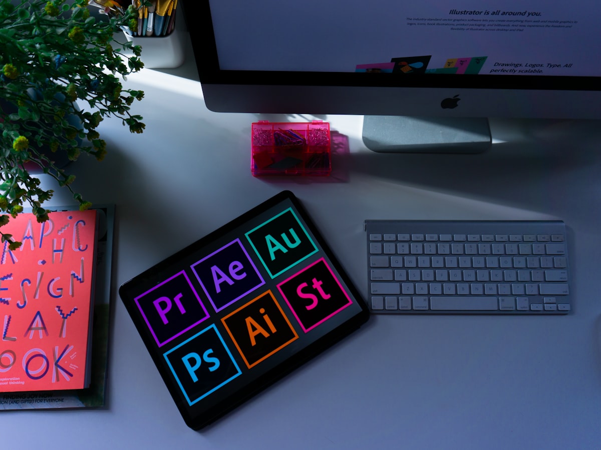 A designer's desk with creative-suite app icons on a tablet.